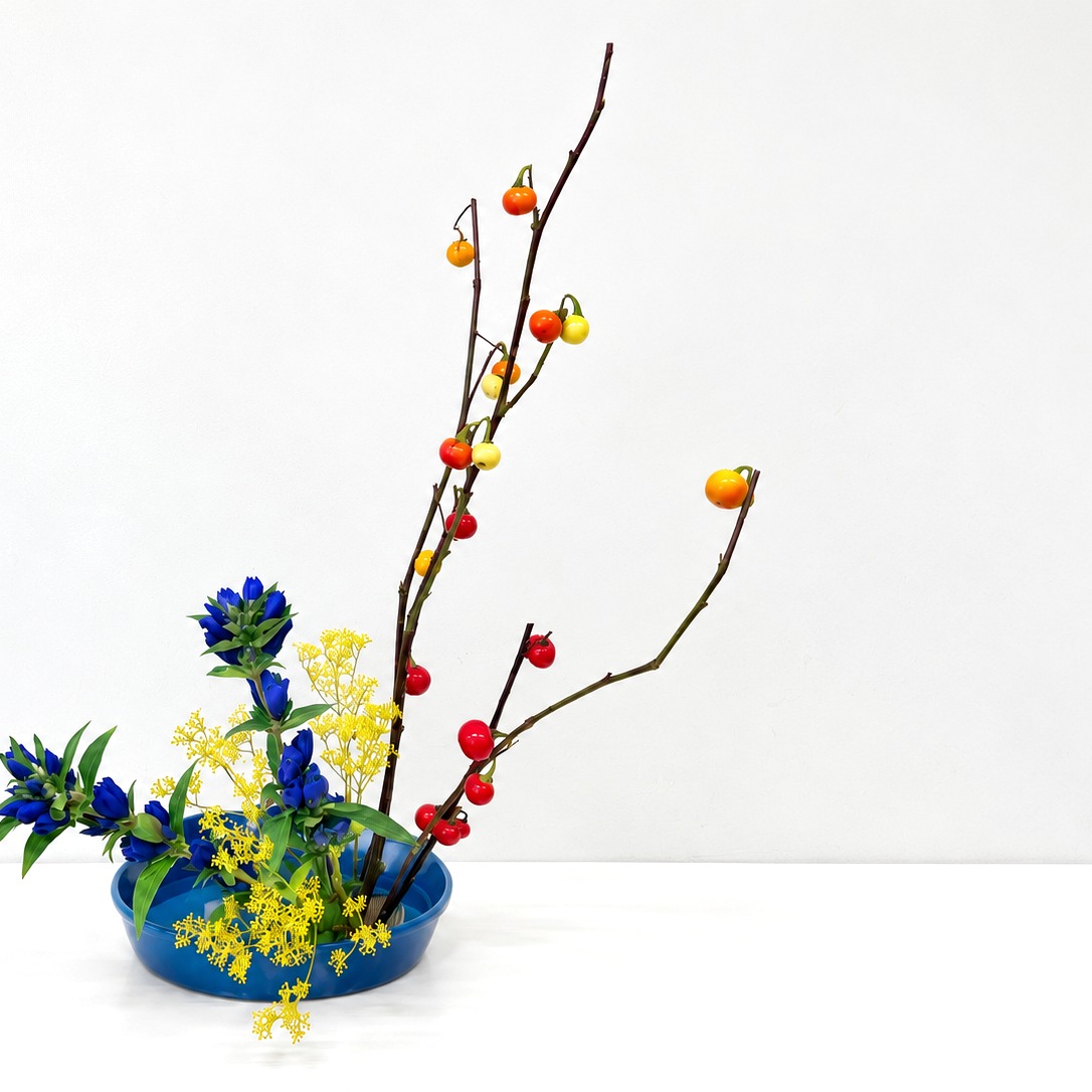 青い器に、枝ものと青や黄色の花をいけた作品